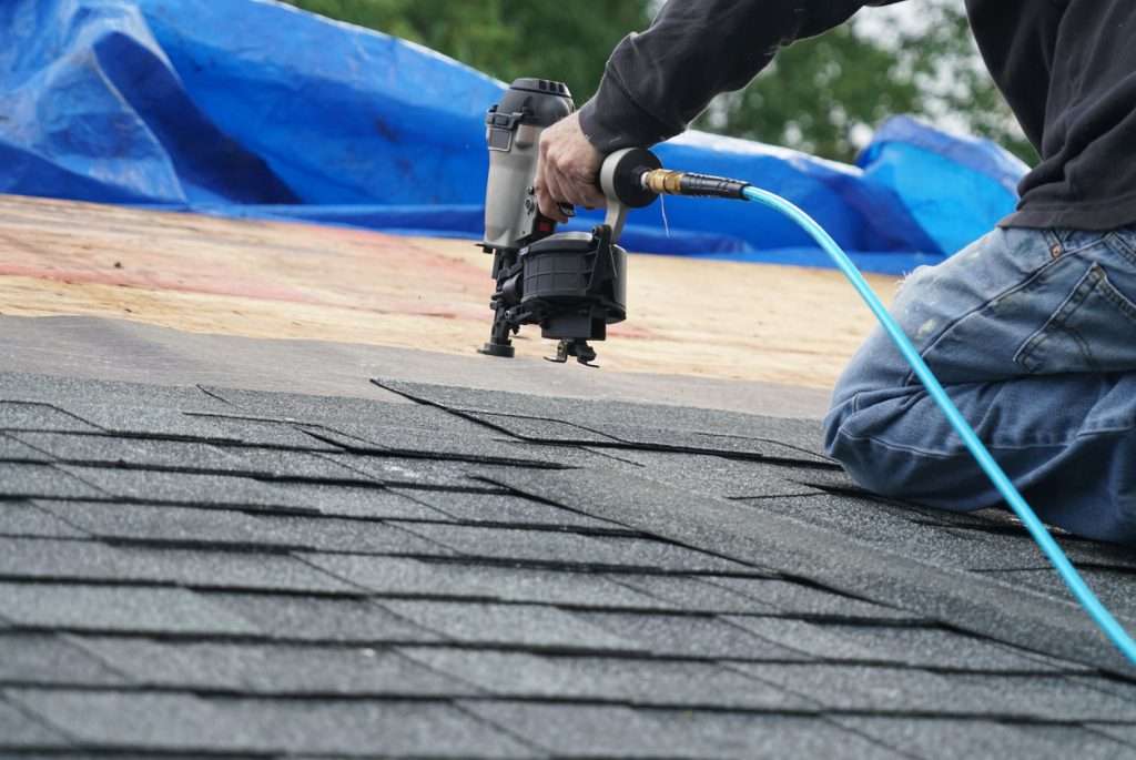 Roofer using a nail gun to install asphalt shingles on a residential roof, highlighting professional and efficient roofing services.
