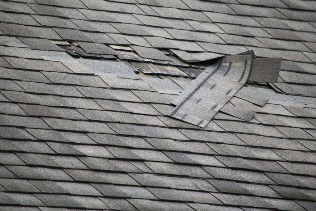 Close-up of a damaged roof with loose shingles exposing underlayment, highlighting the need for prompt professional roof repair.