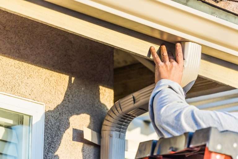 Worker installing a gutter downspout on a house, ensuring proper water drainage and showcasing professional gutter installation services.